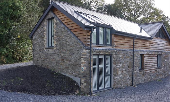 Exterior of Ty Gambo showcasing traditional Welsh stone and contemporary timber cladding, with large shuttered windows.